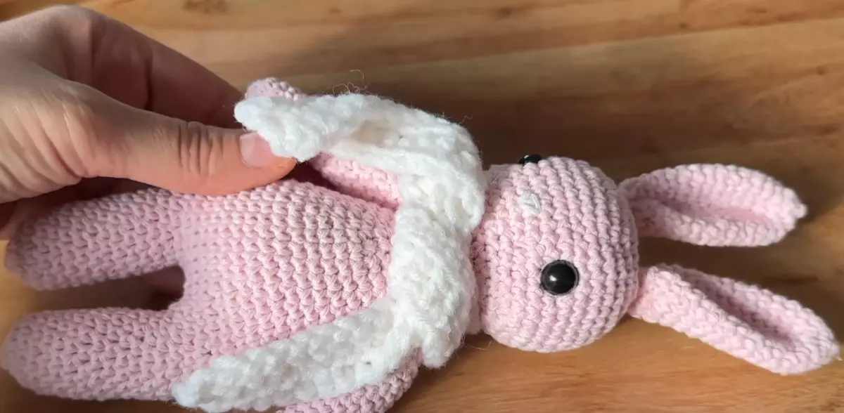 petit lapin rose tricote a la main allonge sur une surface en bois