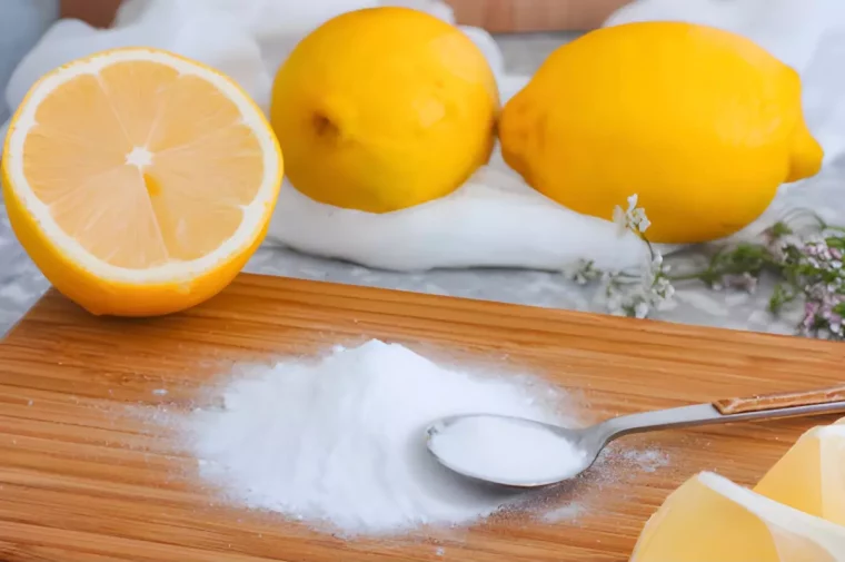 planche a decouper en bois avec un petit tas de bicarbonate dessus et une petite cuillere avec des citron entier et une moitie sur la planche