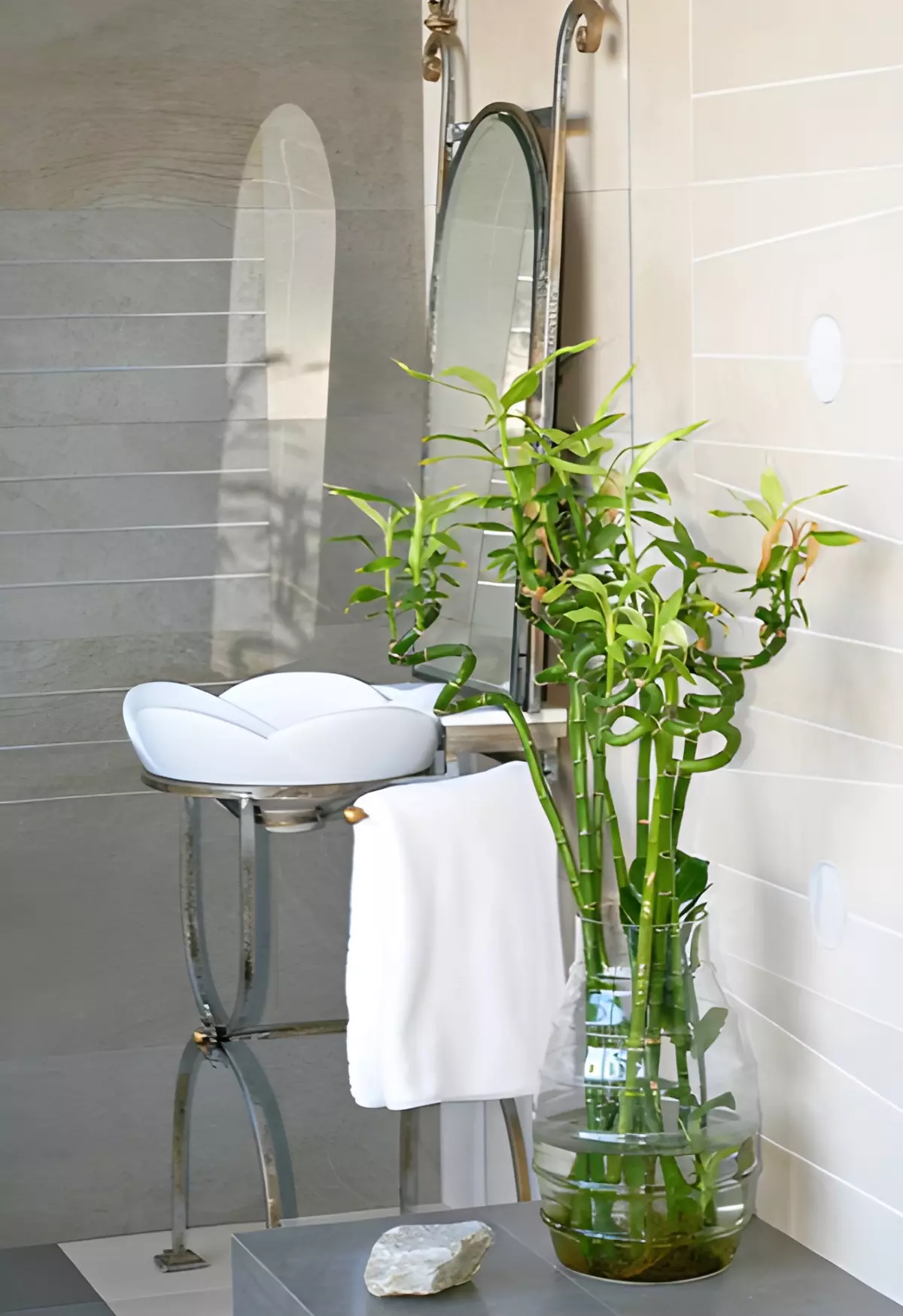 spirale de bamboo dans un vase en verre sur un meuble gris dans une salle de bain a cote d un evier blanc avec un miroir