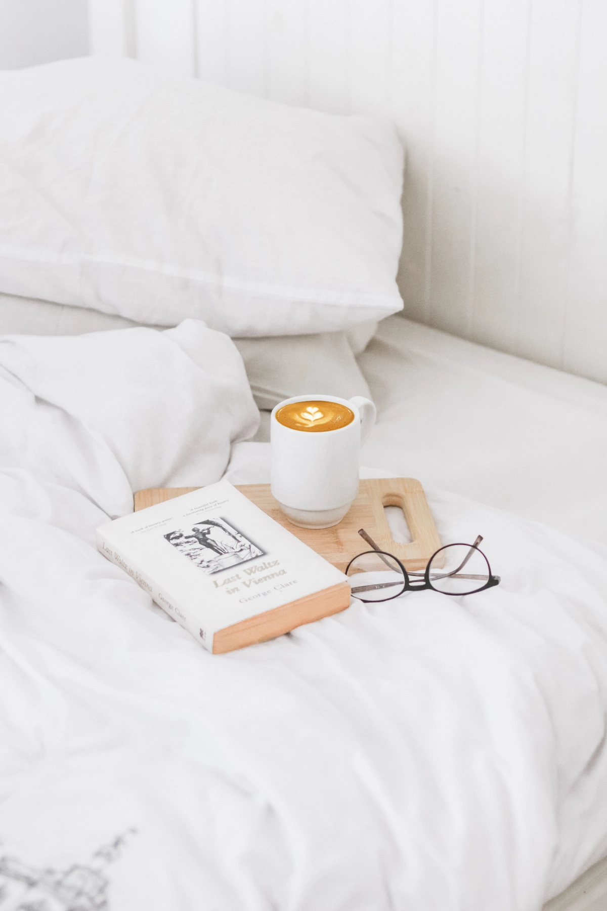 lit blanc draps planche decouper bois tasse cafe livre lunettes de vue