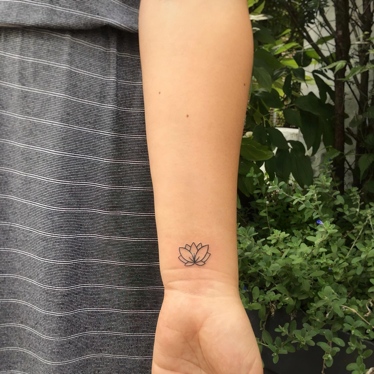 tatouage lotus minimaliste sur poignet main femme ensemble vetements gris et blanc