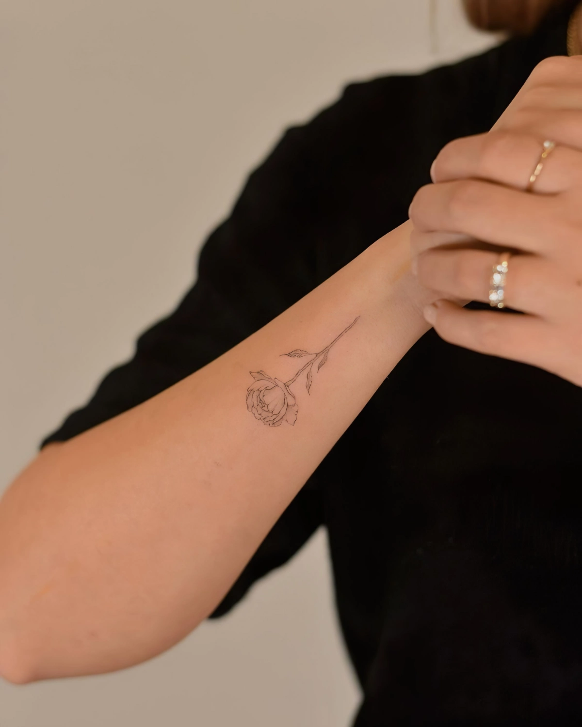 tatouage rose femme dessin minimaliste poignet bijoux bagues or blouse noire