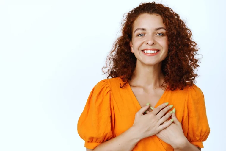 femme en top orange avec les mains sur le coeur