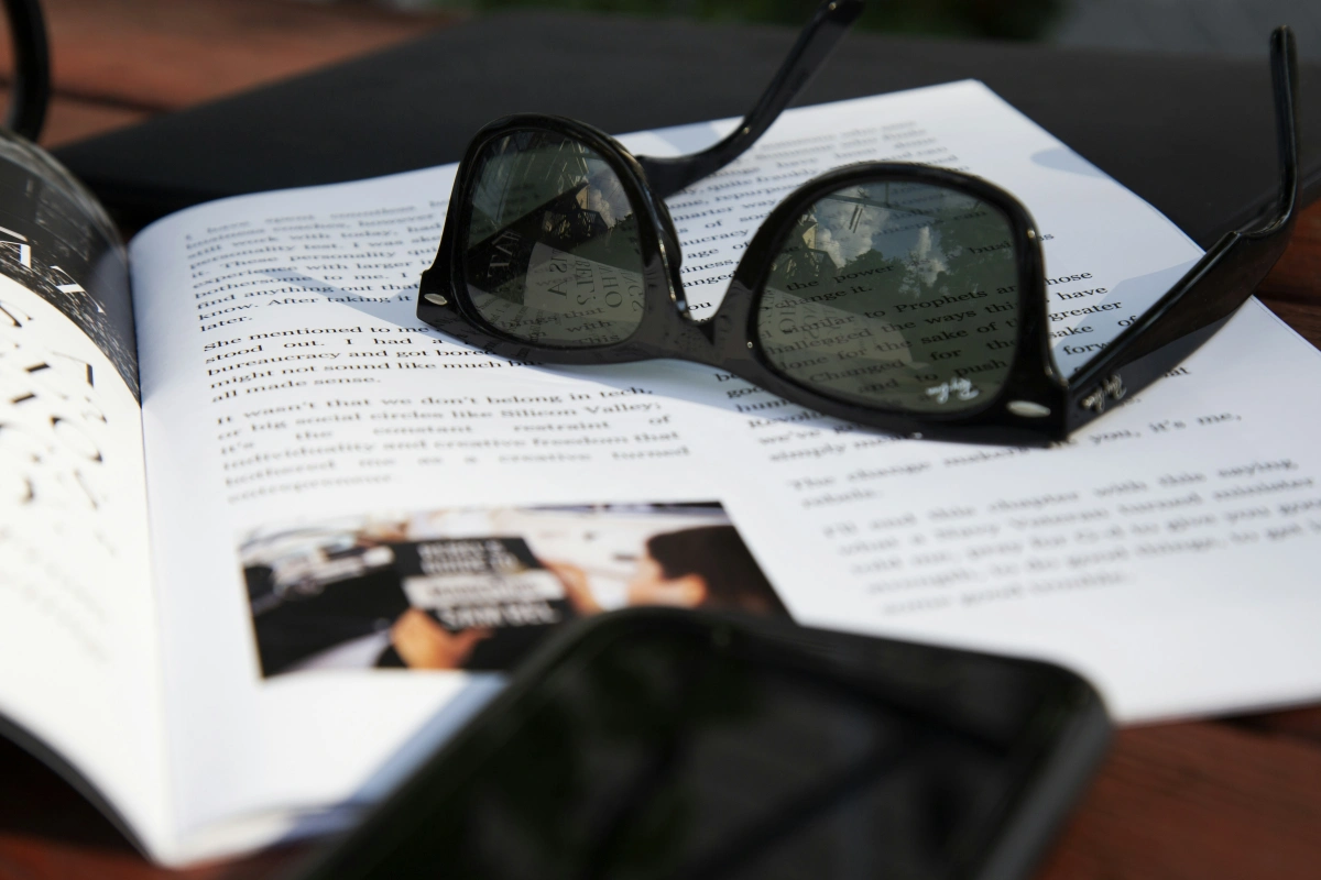 paire lunettes soleil monture noire magazine pages surface table bois