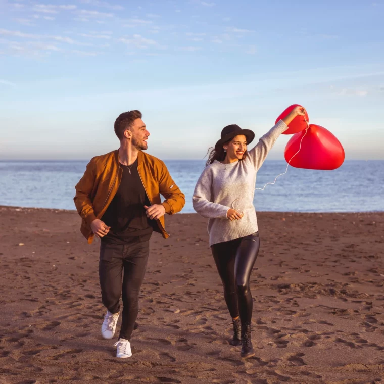 couple running sea shore with heart balloons